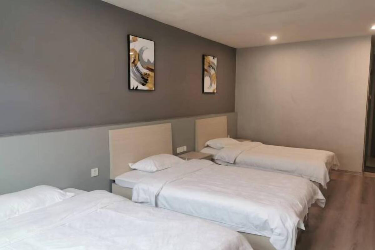 A hotel room with three single beds, a grey wall, and two abstract paintings.
