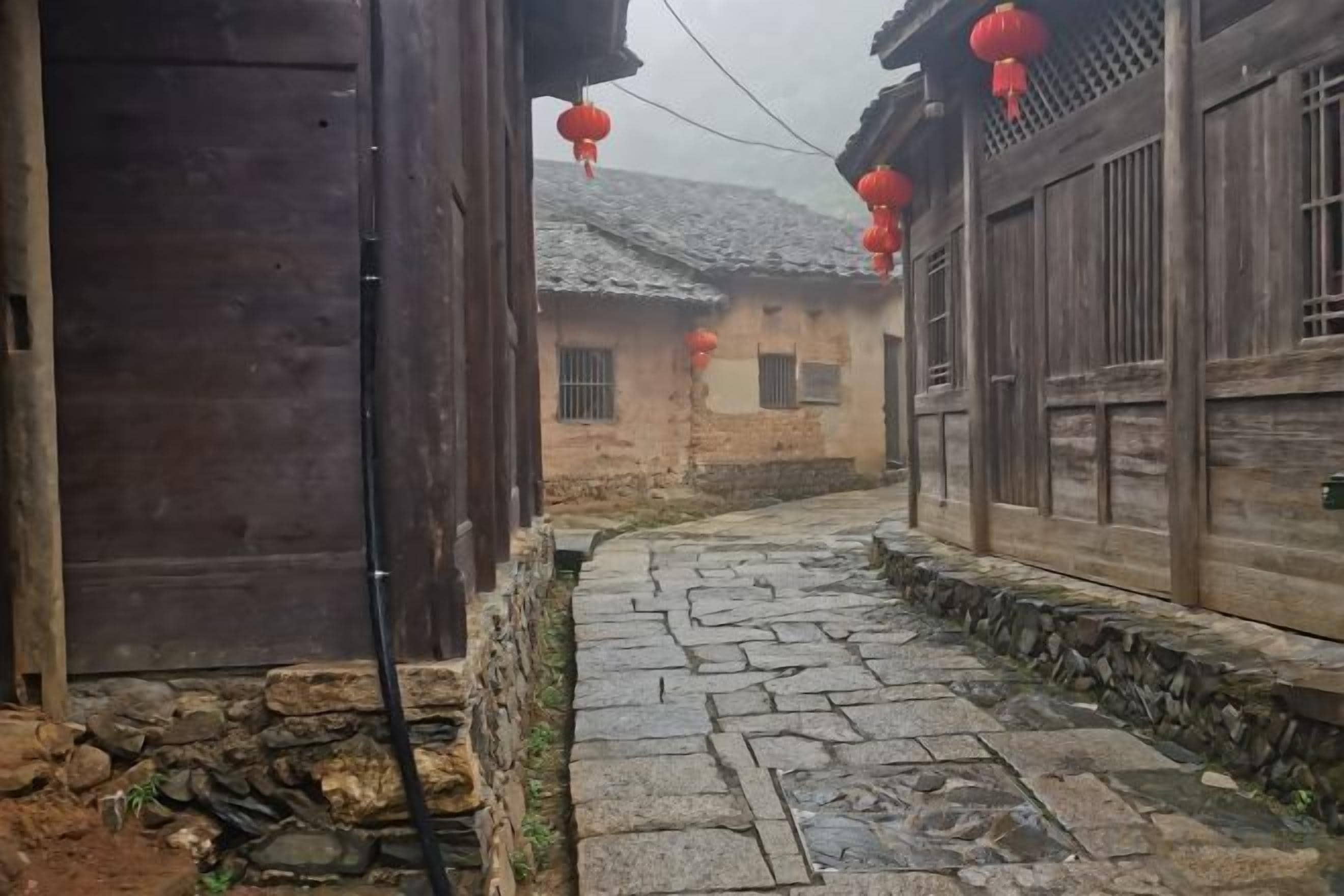 A narrow stone pathway between traditional wooden buildings with red lanterns.