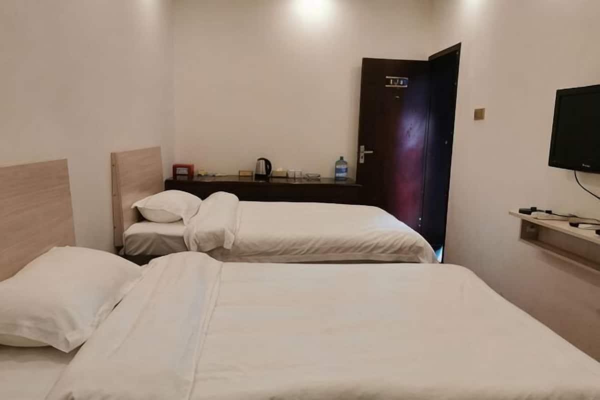 A hotel room with two beds, a wooden headboard, a small table with a kettle, a TV, and a door with a sign.