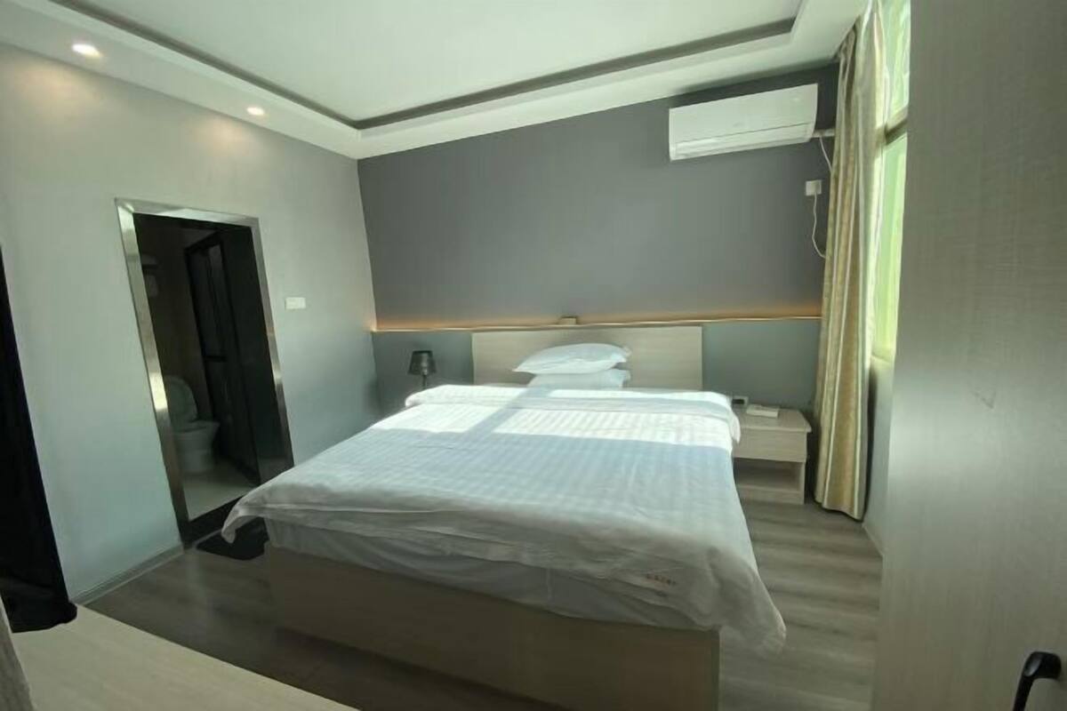 A modern hotel room with a bed, bedside table, and an air conditioning unit.