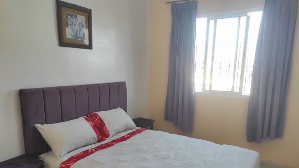 A neatly made bed with a red and white bedspread, a dark headboard, and a small bedside table with a drawer. - Apartment 5 minutes from Anza beach (Agadir)