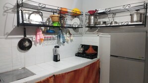 A kitchen with white tiles, a stainless steel refrigerator, a gas stove, and a hanging rack with dishes and kitchen utensils. - Apartment 5 minutes from Anza beach (Agadir)