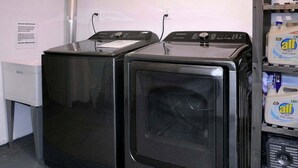 Two black washing machines in a room with a white wall and a shelf with detergent bottles. - Authentic CB, Historic Remodeled Elk Ave Gem! (Crested Butte)