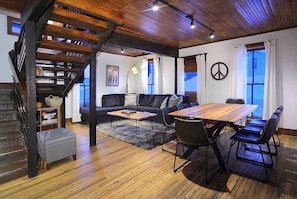 A cozy living area with a wooden staircase, a sofa, a coffee table, and a dining table with chairs.
