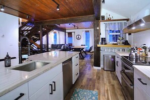 A modern kitchen with a central island, wooden ceiling, and a dining area with a sofa. - Authentic CB, Historic Remodeled Elk Ave Gem! (Crested Butte)