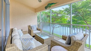 Un balcón con muebles de mimbre, un ventilador de techo y vistas a un lago con árboles.