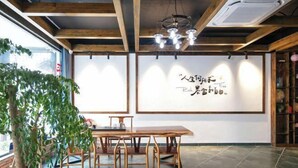 A room with a wooden ceiling, a dining table with chairs, a large window, and a wall with calligraphy art.
