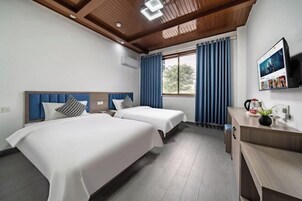 Una habitación de hotel con dos camas, techo de madera, un escritorio con una planta y un televisor en la pared.