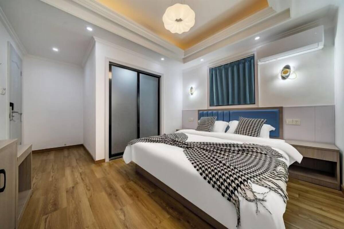 Ein modernes Schlafzimmer mit einem großen Bett, Holzboden, einer Deckenleuchte und einer Wandlampe.