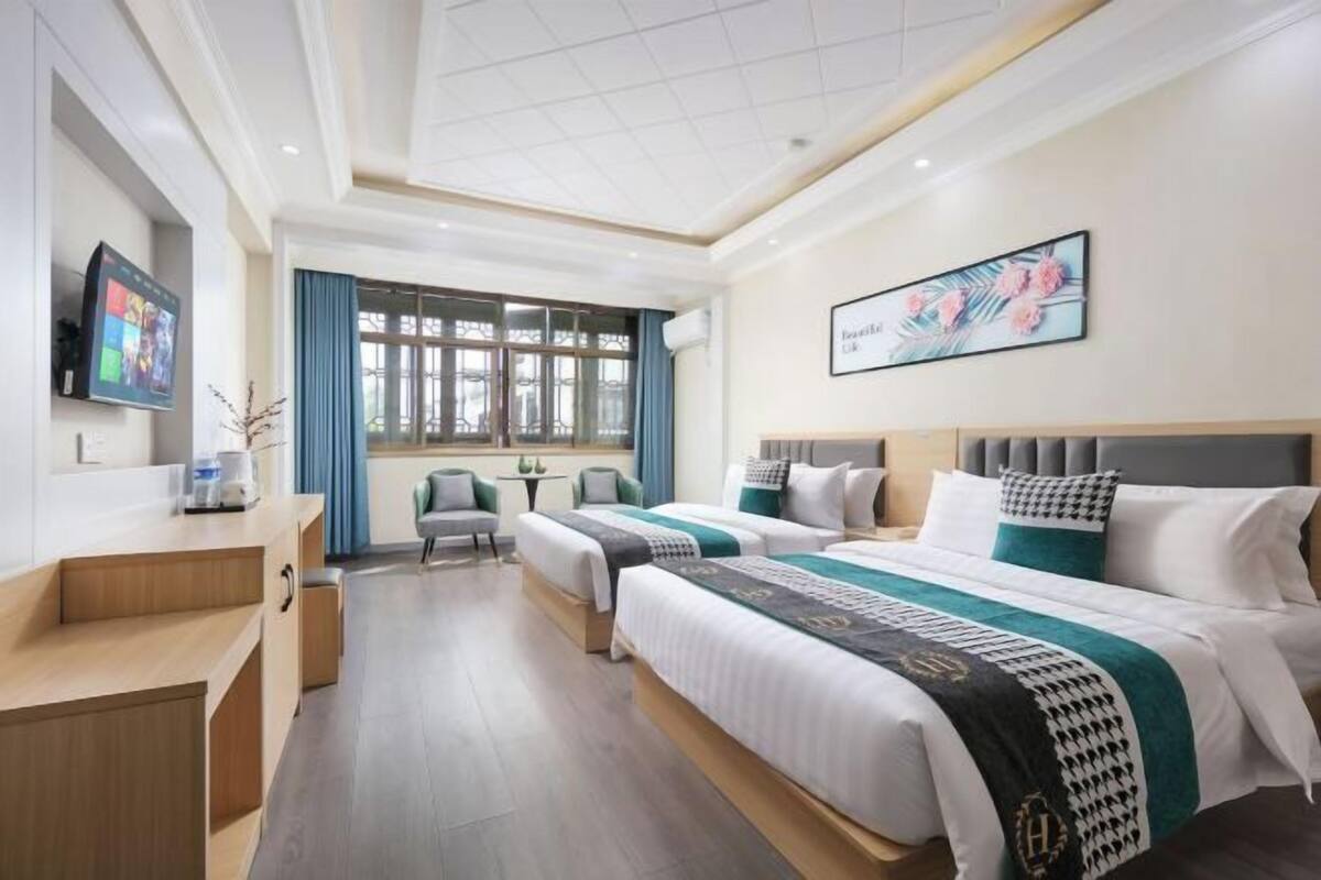Ein Hotelzimmer mit zwei Betten, einem Schreibtisch, einem Fernseher und einem Fenster mit Vorhängen.