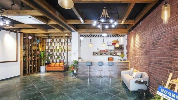 A spacious room with a high ceiling, exposed wooden beams, a brick wall, and a seating area with a sofa and bar stools.