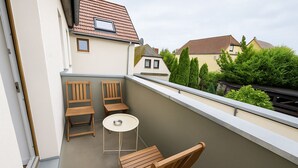 Un balcone con due sedie di legno e un tavolino rotondo, con vista su una zona residenziale con case e alberi.