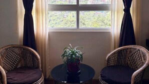 A room with a large window, two wicker chairs, a small table, and a potted plant. - Mazong Crest (Gangtok)