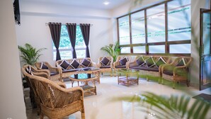 A spacious lounge area with wicker furniture, large windows, and potted plants. - Mazong Crest (Gangtok)