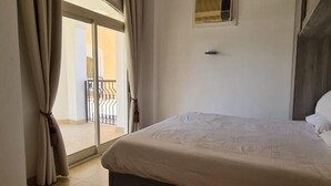 Ein Schlafzimmer mit Bett, einem Fenster mit Vorhängen, einem Deckenventilator und Blick auf einen Balkon.