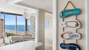 Una habitación con vistas a la playa, una mesa de comedor y una pared con un cartel que dice 'The Beach is My Happy Place'.