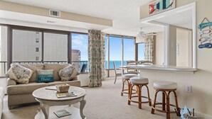Amplia sala de estar con balcón, un sofá con almohadones decorativos, una mesa de centro redonda y un juego de comedor.