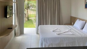 A hotel room with a bed, a TV mounted on the wall, and a view of a garden. - Pousada Água Mar (Grossos)