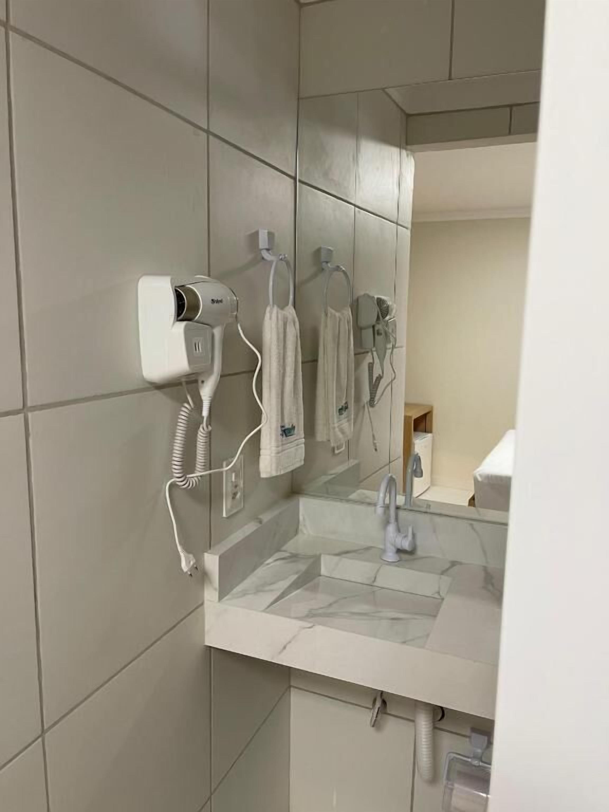 Un baño con espejo, un lavamanos y dos secadores de pelo fijados en la pared.