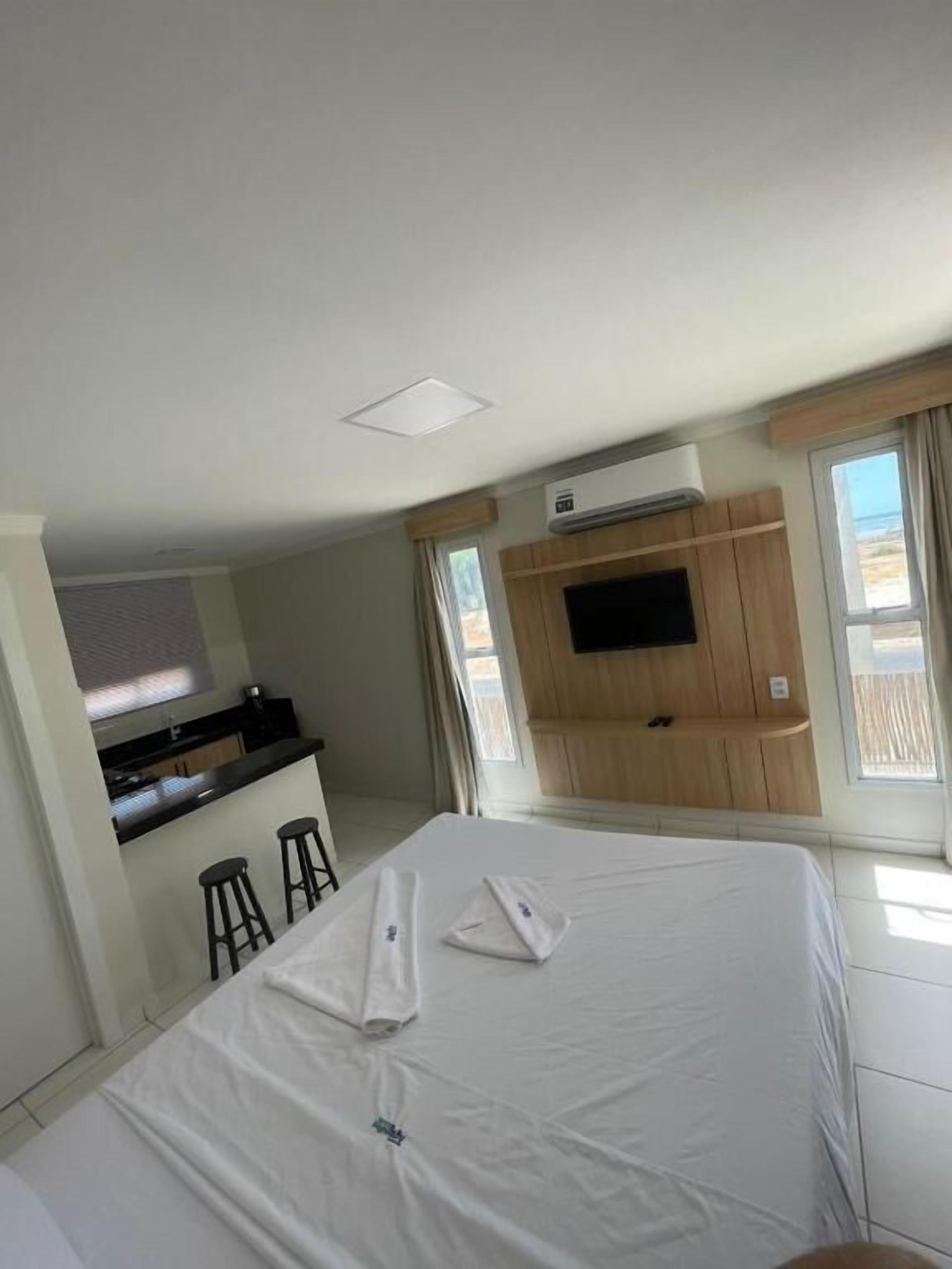 A hotel room with a bed, a TV mounted on the wall, a kitchenette, and a window.