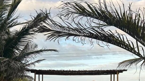 A pathway leading to a covered area with a view of the sky and palm trees. - Pousada Água Mar (Grossos)