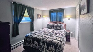 Een slaapkamer met een bed, twee bedlampen, een raam met gordijnen en een aan de muur hangend schilderij.