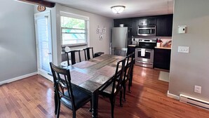 A dining area with a wooden table and chairs, a kitchen with modern appliances, and a window with blinds. - Newly refreshed four bedroom, three full bath multilevel condo (Sugar Mountain)