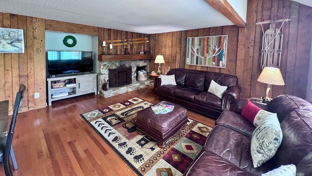 A cozy living room with a stone fireplace, leather sofa, and a television. - Newly refreshed four bedroom, three full bath multilevel condo (Sugar Mountain)