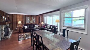 A spacious living room with a large wooden dining table, leather sofas, and a stone fireplace. - Newly refreshed four bedroom, three full bath multilevel condo (Sugar Mountain)