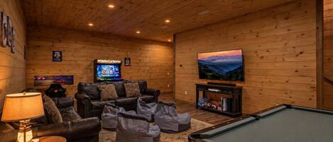 Una habitación acogedora con mesa de billar, sofás de cuero, televisor y juegos de arcade.