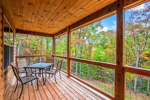 A wooden deck with a table and chairs, overlooking a forest with autumn foliage.