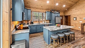 A modern kitchen with blue cabinets, a granite countertop, and a central island with bar stools.