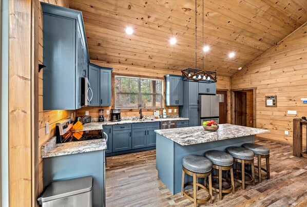 A modern kitchen with blue cabinets, a granite countertop, and a central island with bar stools. - Luxe 4BR w/Firepit*Hot Tub*Game Room*Comm Pool (Sevierville)
