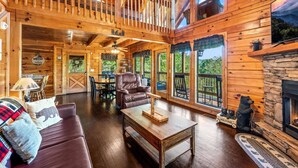 A cabin interior with a wooden interior, a fireplace, a dining area, and large windows. - 2BR w/Hot Tub*Fireplace, MTN View, Community Pool! (Sevierville)