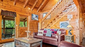 A wooden cabin interior with a staircase, a leather sofa, a coffee table, and a painting of a bear. - 2BR w/Hot Tub*Fireplace, MTN View, Community Pool! (Sevierville)