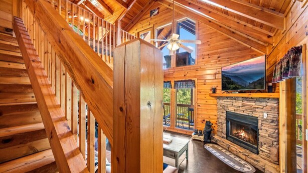 A wooden cabin interior with a stone fireplace, a wooden staircase, and a large window overlooking a scenic landscape. - 2BR w/Hot Tub*Fireplace, MTN View, Community Pool! (Sevierville)