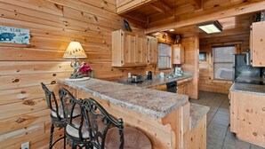 A wooden cabin interior with a kitchen area, including a granite countertop, wooden cabinets, and a dining table with chairs. - 2BR Cabin w/MTN Views*Hot Tub*Games*Community Pool (Sevierville)