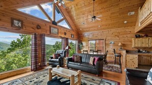 A spacious cabin with a large living area, a dining table, and a kitchen. - 2BR Cabin w/MTN Views*Hot Tub*Games*Community Pool (Sevierville)