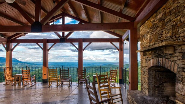 A covered outdoor seating area with wooden chairs and a stone fireplace. - 2BR Cabin w/MTN Views*Hot Tub*Games*Community Pool (Sevierville)