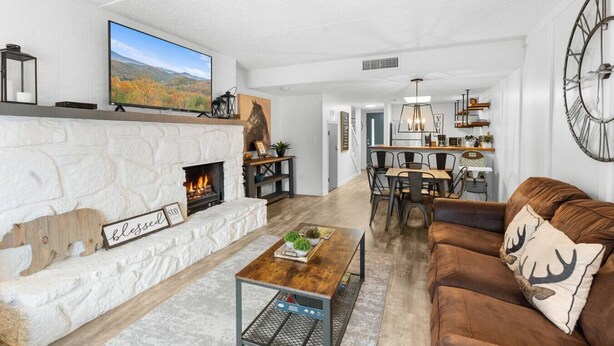 Una sala de estar moderna con chimenea, un comedor y una cocina visible al fondo.