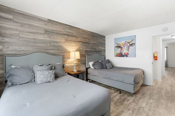 A bedroom with two beds, a wooden accent wall, a painting, and a fire extinguisher.