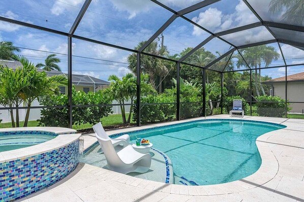Une piscine dotée d’une enceinte en verre, entourée d’une végétation luxuriante et surplombée par un ciel dégagé.