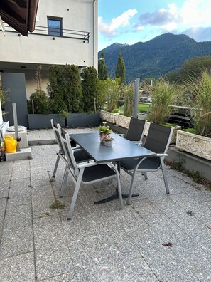 An outdoor patio with a table and chairs, surrounded by plants and a mountain view. - Central but quietly located, lovely and well furnished flat in Balzers. (Balzers)