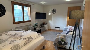 Une chambre à coucher avec un lit, un bureau, une télévision, une lampe et une fenêtre.