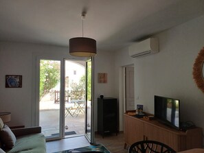 A living room with a sofa, a television, a cabinet, and a sliding glass door leading to an outdoor area. - "An Endless Summer"! Apartment with a courtyard, a 5-minute walk from the ocean. (Saintes-Maries-de-la-Mer)