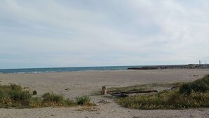 En strand med en stenig kustlinje, en stig som leder ner till vattnet och en brygga en bit bort.