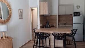 Ett modernt kök med en bänkskiva i trä, en inbyggd mikrovågsugn och ett kylskåp. Det finns två svarta barstolar och ett matbord i trä. En stor, grå hänglampa hänger ovanför bordet.