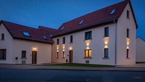 A modern two-story building with a red-tiled roof and multiple illuminated windows. - Lux Suites Leipzig Paradise Apartment (Leipzig)