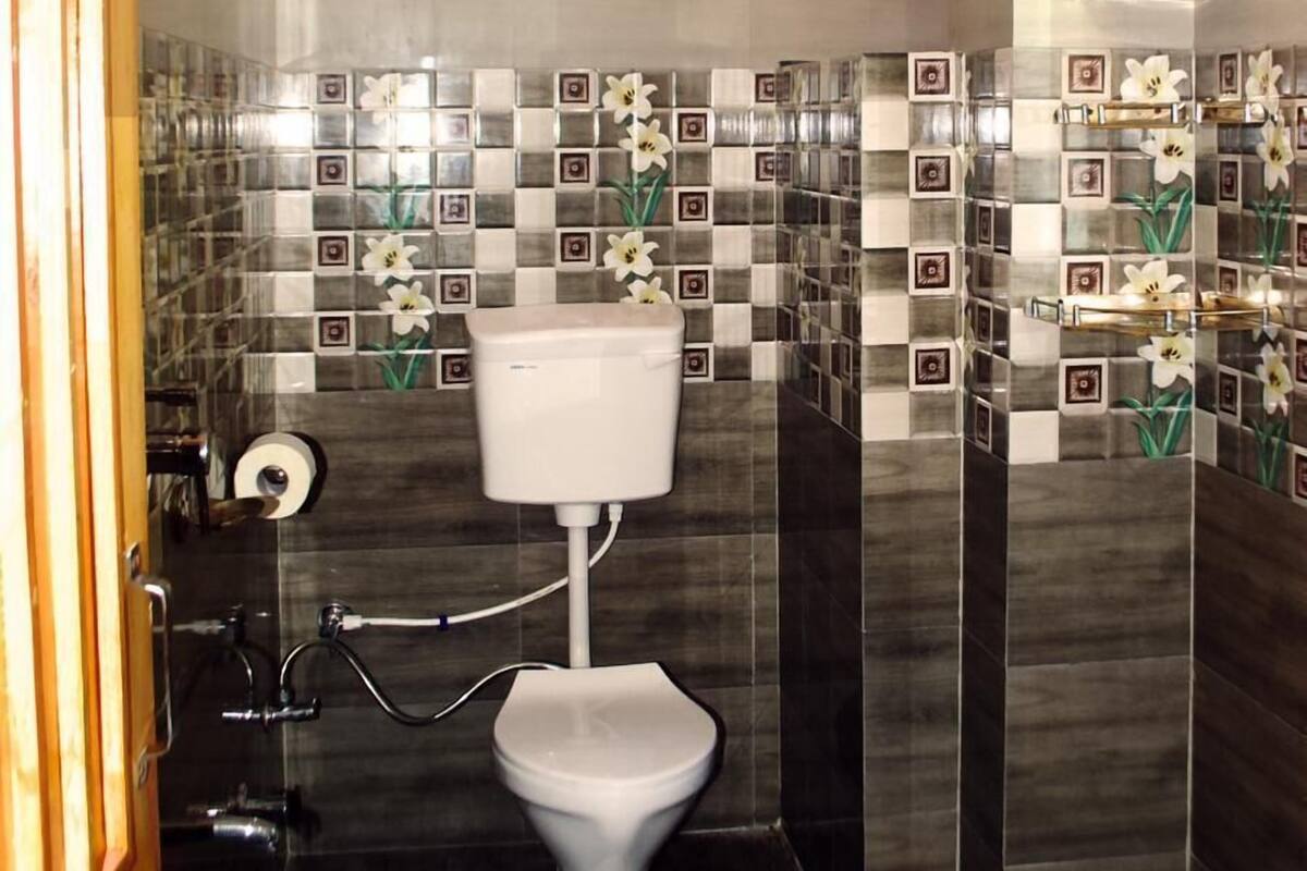 A bathroom with a toilet, a hand dryer, and a showerhead.