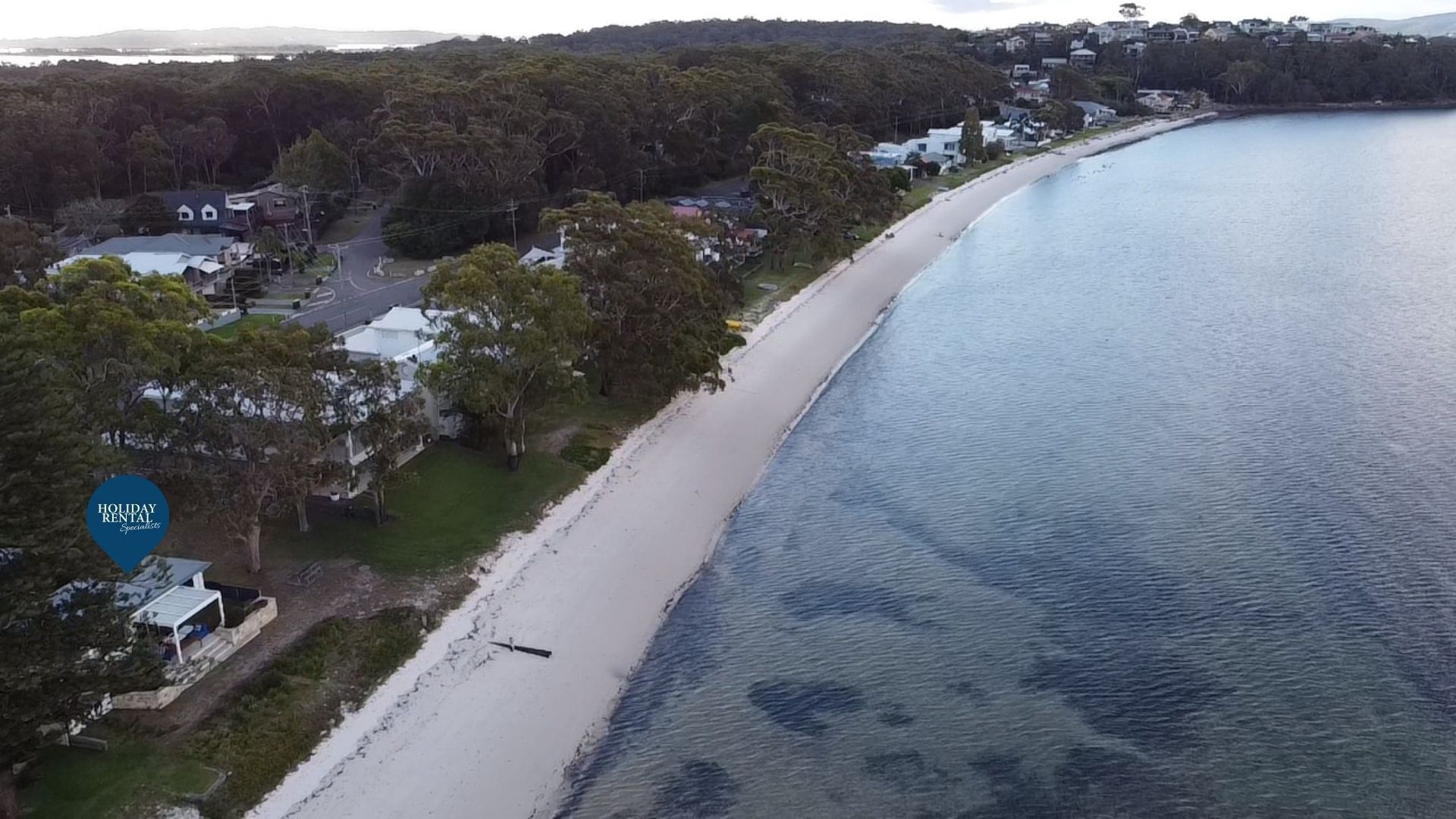 Une vue aérienne d’une zone côtière avec une plage, des maisons et une route.